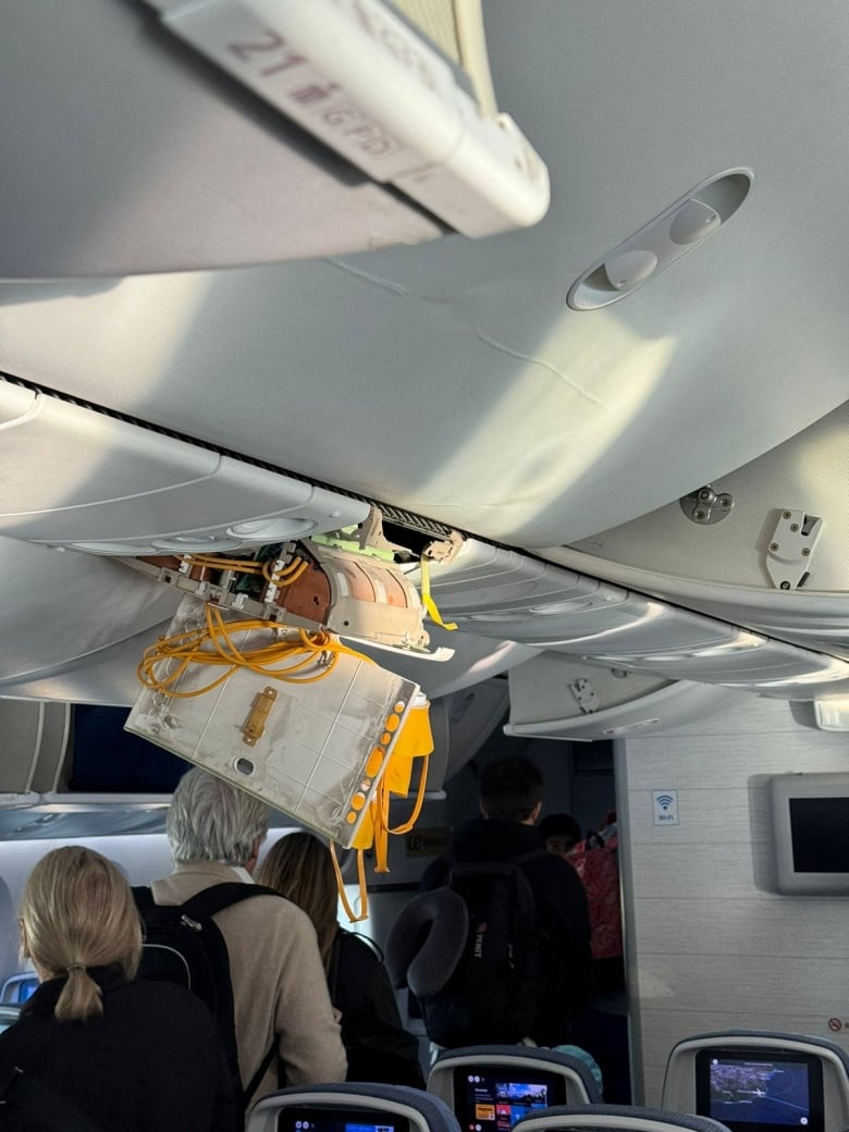 A broken piece of the plane's cabin ceiling dangles as passengers move down the aisle.