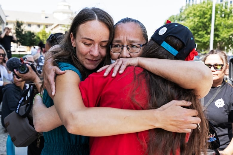 Three people embrace.