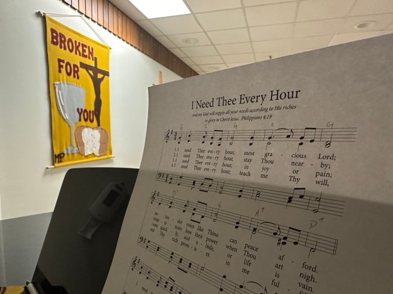 A sheet of music on a piano is shown near a yellow banner depicting Christ's crucifixion.