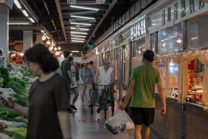 An elderly man rides a tricycle through a Chinese market