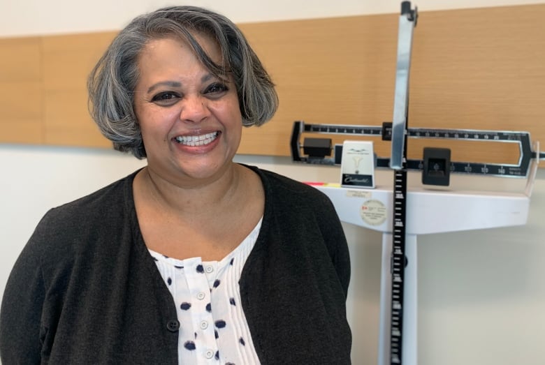 A woman with a big, broad smile looks at the camera. Behind her is a scale. 