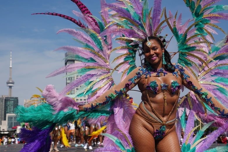 A woman wearing a huge feathery ensemble smiles for a photo at the Toronto Caribbean Carnival.