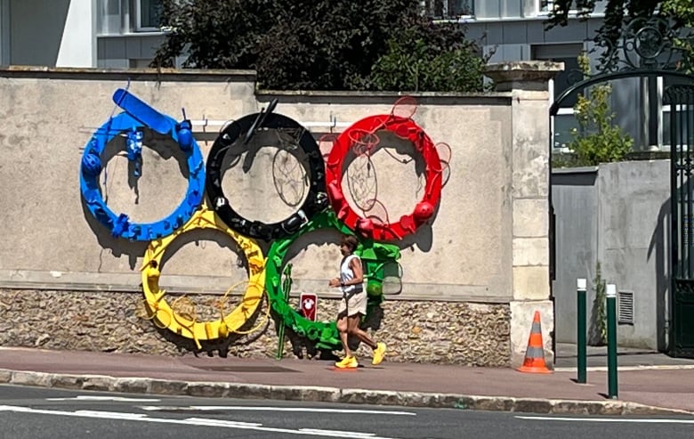 A woman  runs  past  a sculpture of the olympic rings