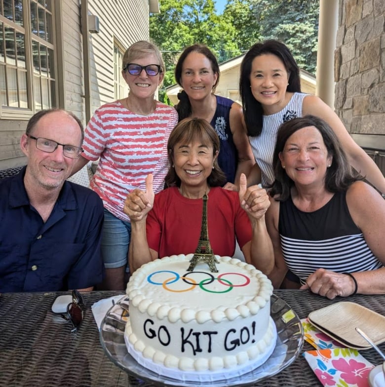 Six  people gather around a  cake that  says go kit go!