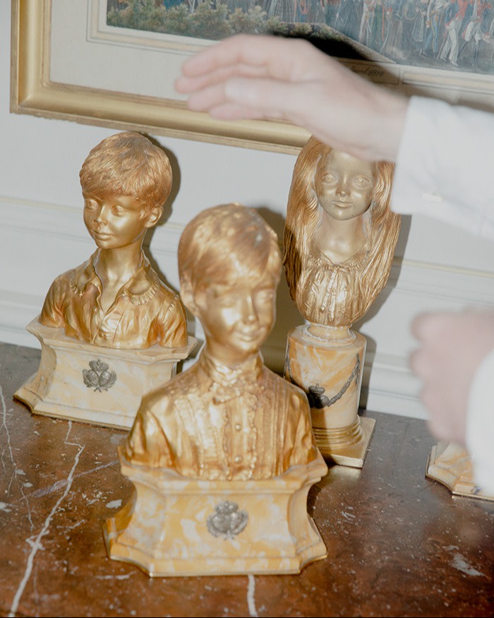 A pair of hands reaching out to touch three gold busts of children sitting on a table