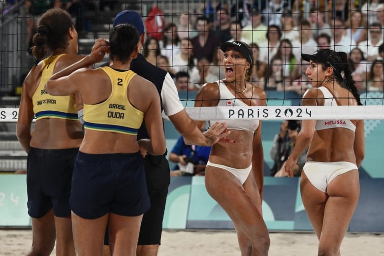 Four female beach volleyball players are seen close to the net, in an argument, while an official appears to mediate the situation.