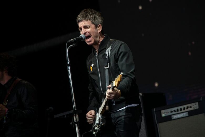 A man singing into a microphone and playing a guitar performs onstage.