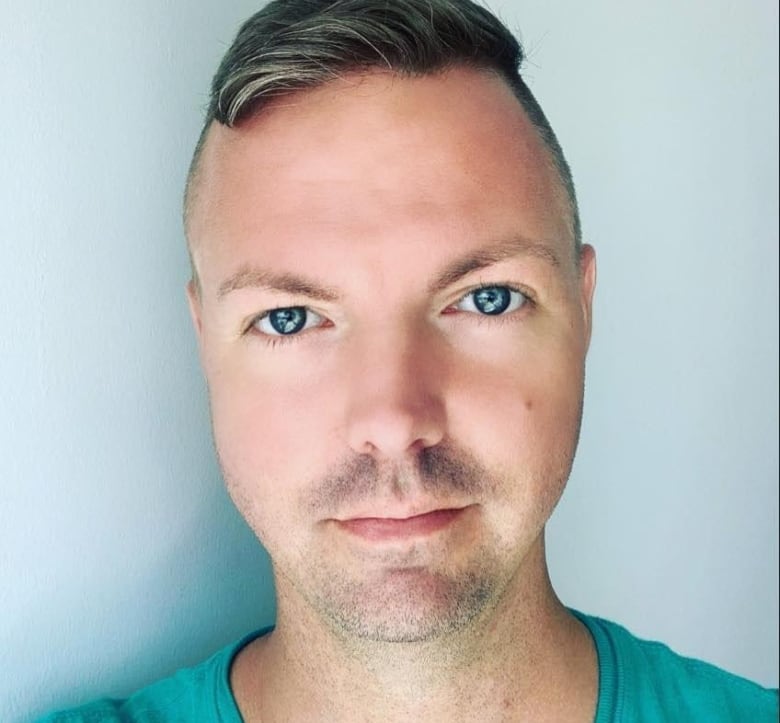 A portrait of a man wearing a light green t-shirt, in front of a grey background. 