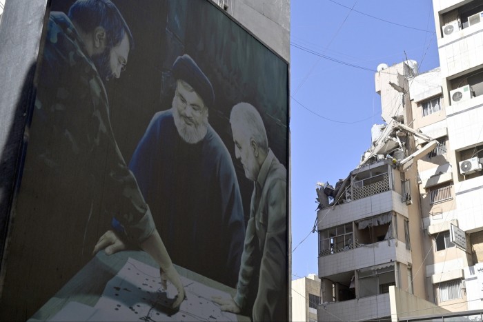 A billboard depicting late Hizbollah senior member Imad Mughniyeh (L), Hizbollah leader Hassan Nasrallah (C), and late Iranian Major-General Qassem Soleimani (R), next to a damaged building at the site of an Israeli strike the previous day in Beirut