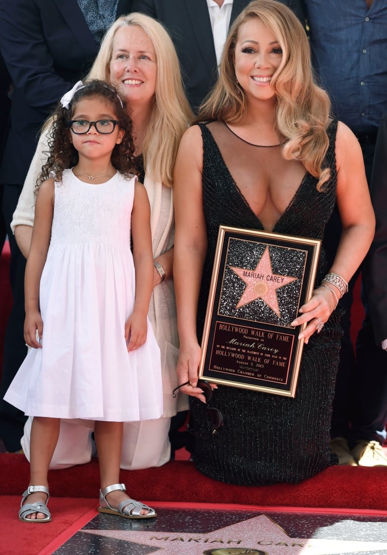 An older woman and young girl pose next to a woman kneeling before a star emblazened on the ground and holding a plaque also bearing a star.