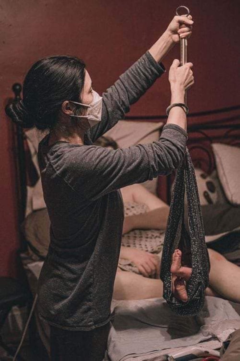 A woman in a surgical mask weighs a newborn baby using a sling scale.