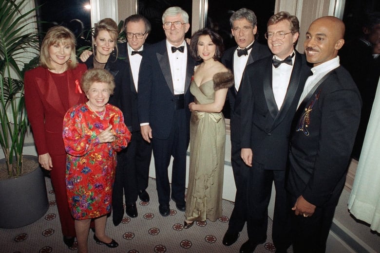 A group of men and women in formalwear pose together in a half-circle for a group photo