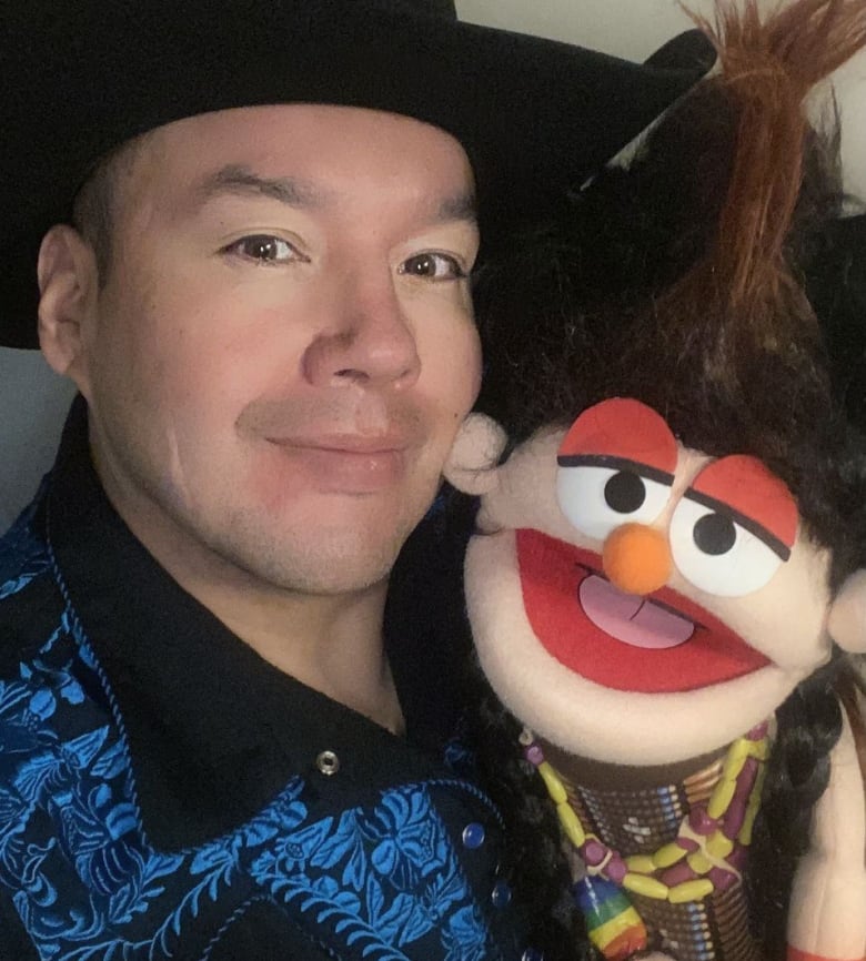 A man in a black cowboy hat holds a puppet.