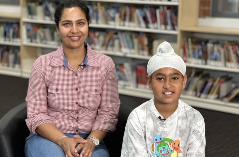 A woman in a checked button-up shirt sits in a school library next to her 10-year-old son.