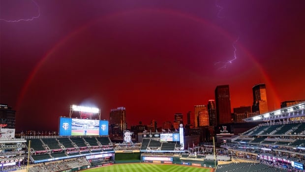 A pink sky with a rainbow and lightning over a baseball stadium