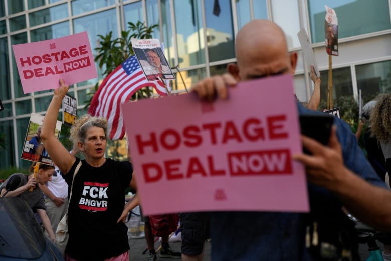 People hold pink signs with red lettering that reads "Hostage Deal Now." 