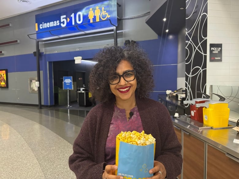 A woman stands with popcorn in a movie theatre.