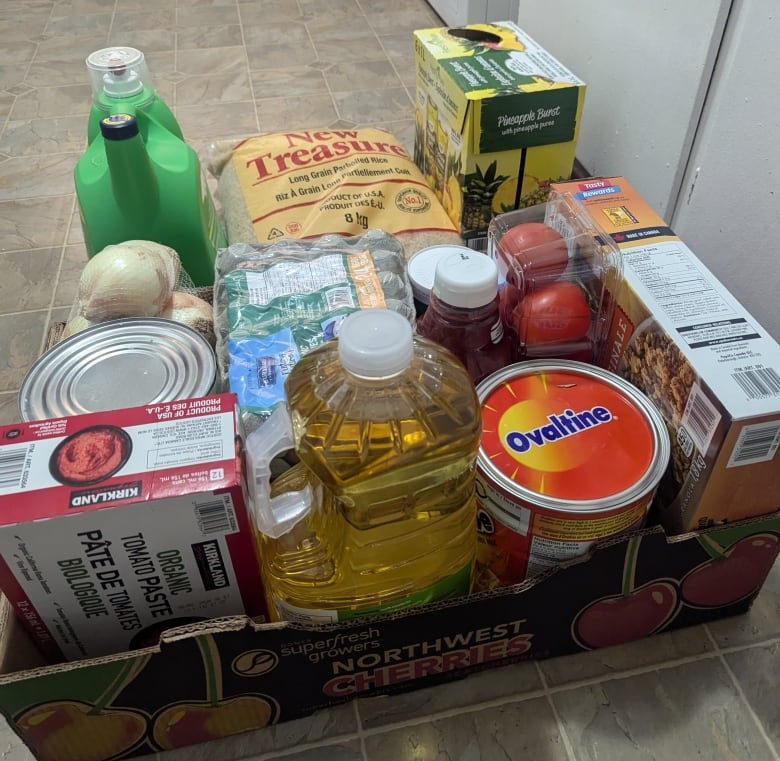 A box with food items including oil, tomatoes, and cereal.