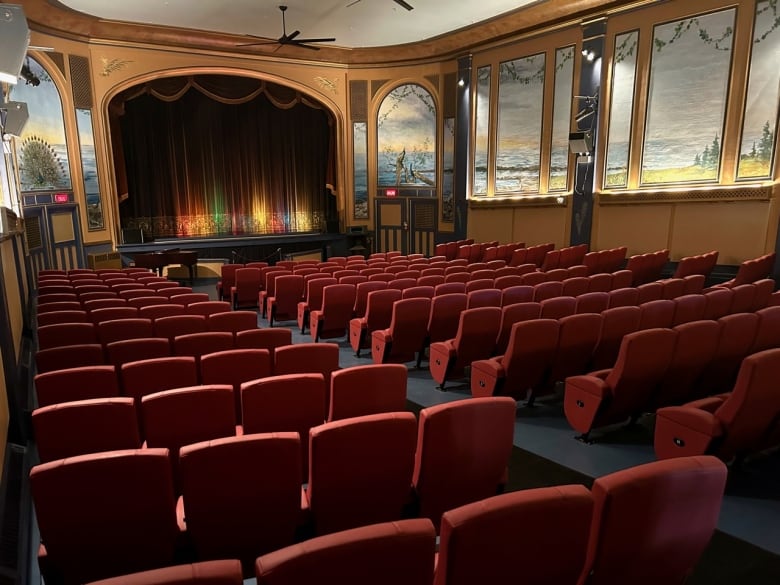 A grand old movie theatre with red seats and murals showing peacocks and outdoor scenery painted on the walls.