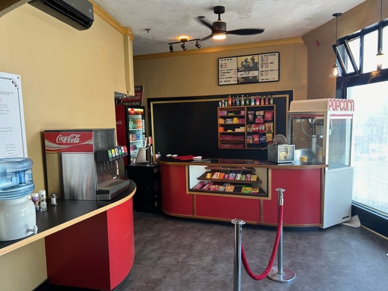 An old-fashioned theatre concession stand features a red counter with a display window for candy and a popcorn machine. 