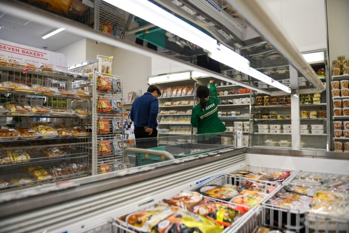 A worker restocks shelves while a customer shops at a branch of 7-Eleven