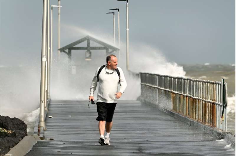 A man walks along a pier leading into Port Phillip Bay in Melbourne as winds of more than 110 kilometres (68 miles) per hour lash the region