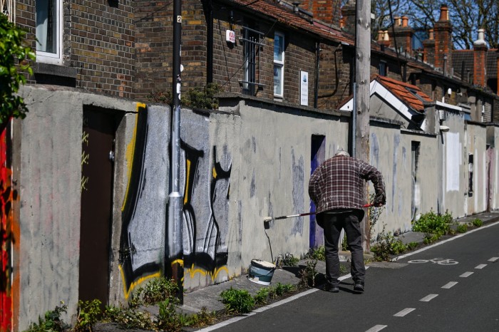 A man is cleaning a wall with graffiti by painting over it