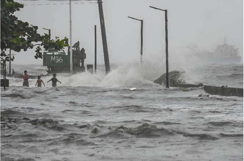 People frollick in storm surge along Manila Bay during heavy rain brought by Tropical Storm Yagi