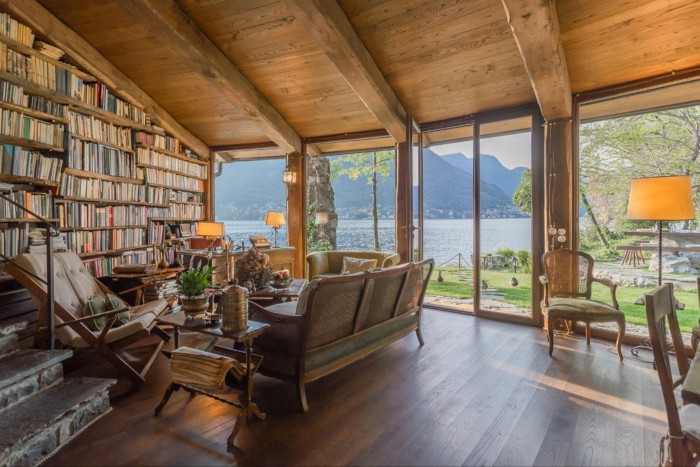 A rustic living room with a wall full of books, overlooking Lake Como and mallards on the lawn