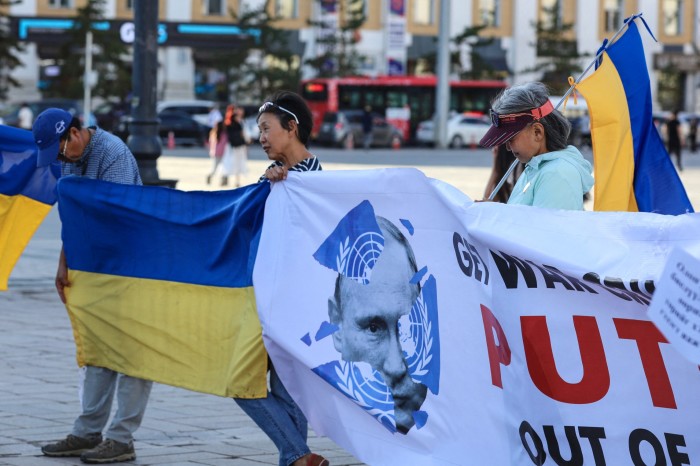 Three people holding Ukrainian flags and a banner