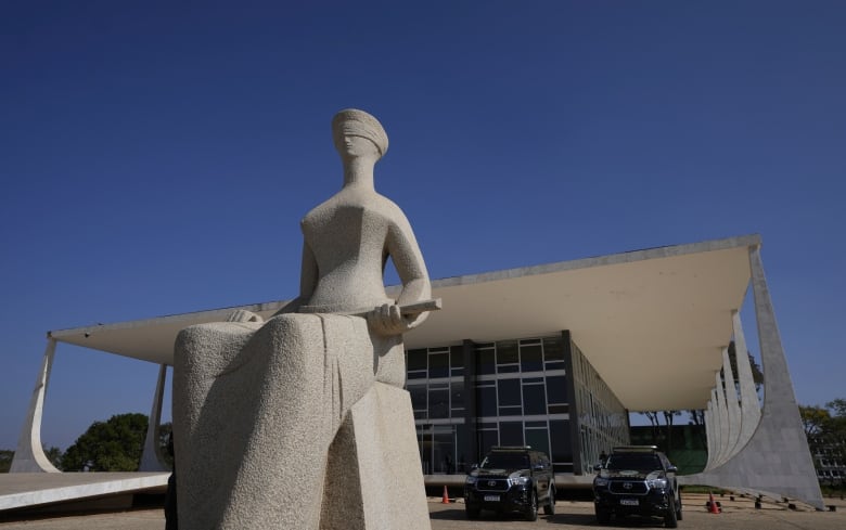 A statue of a seated and blindfolded person is seen in front of a building.