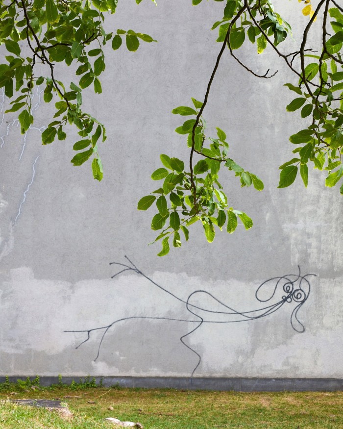 ‘Undine’ by Harald Naegeli: a horizontal stick figure on a grey wall. In the foreground a tree’s branches a bobbing above it 