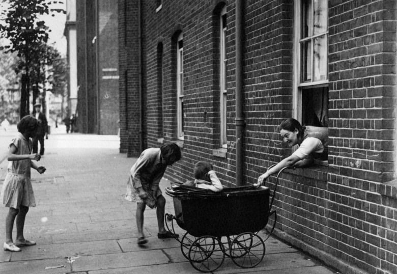 A woman leans out of a window to push a carriage with a child in it