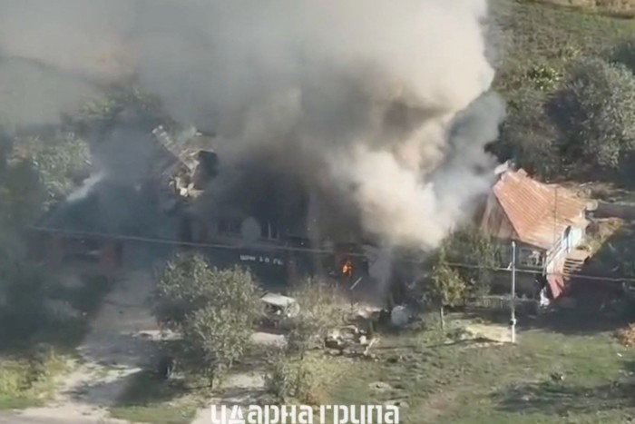 Smoke billows from a building on fire. The surrounding area appears to be rural with some vegetation