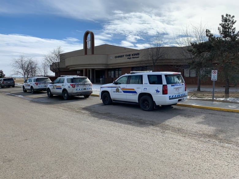 Police vehicles are lined up outside a brown building with a sign that says "Christ the King High School."