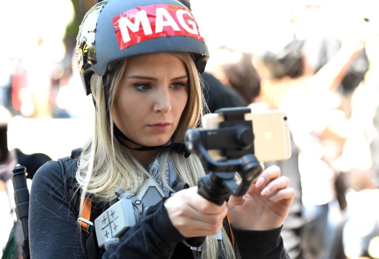 A woman in a MAGA helmet live streams with her iPhone at a rally.