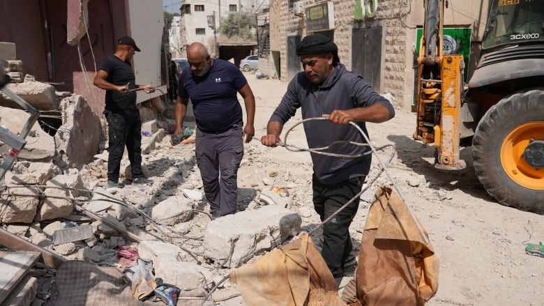 People remove rebar, bricks and other debris from the site of a destroyed building.