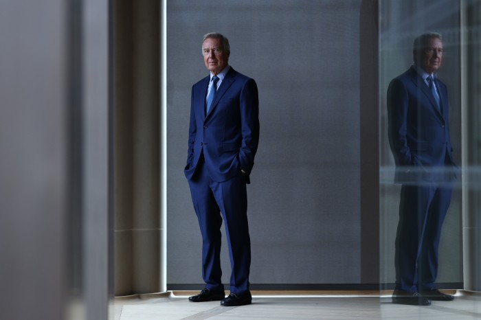 A middle-aged man in a blue suit stands in a corridor