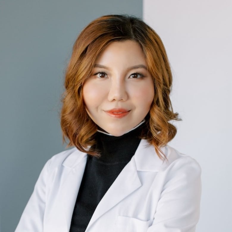 A headshot of a person who is wearing a medical jacket over a turtleneck.