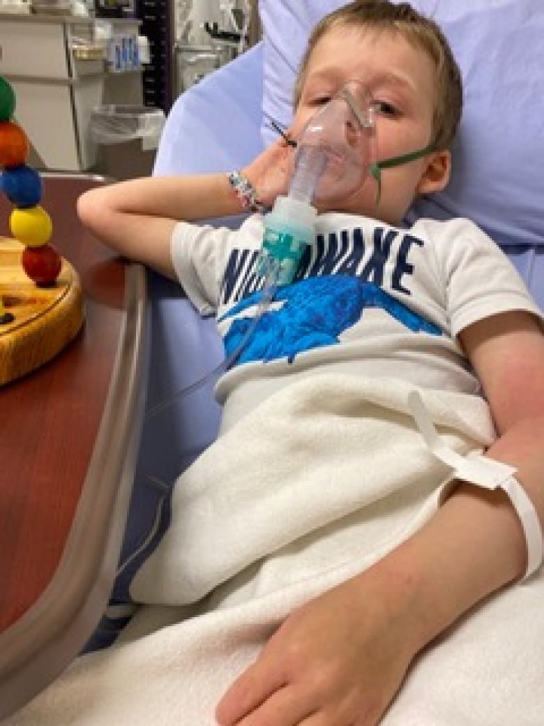 A child lies in a hospital bed with a breathing tube over his face. 