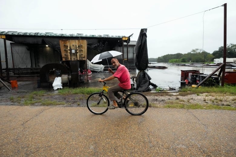 A man rides a bike while carrying an umbrella.