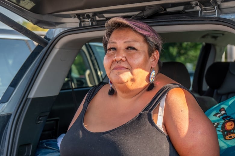 A person is seen sitting on the edge of a vehicle's open trunk.