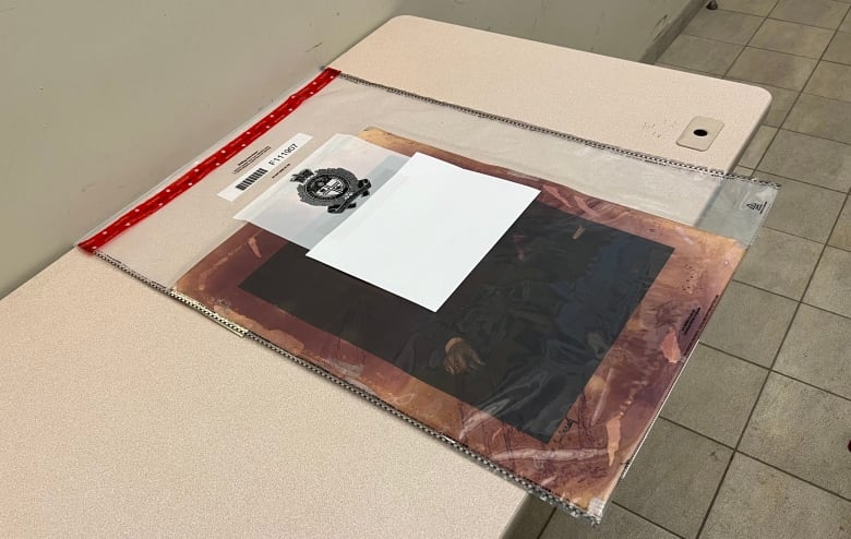 A photograph discoloured with burgundy dye is shown in a plastic sleeve on a white table.