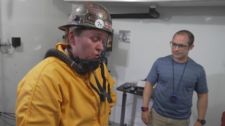 Woman in yellow jumpsuit exhales as man with timer looks on.