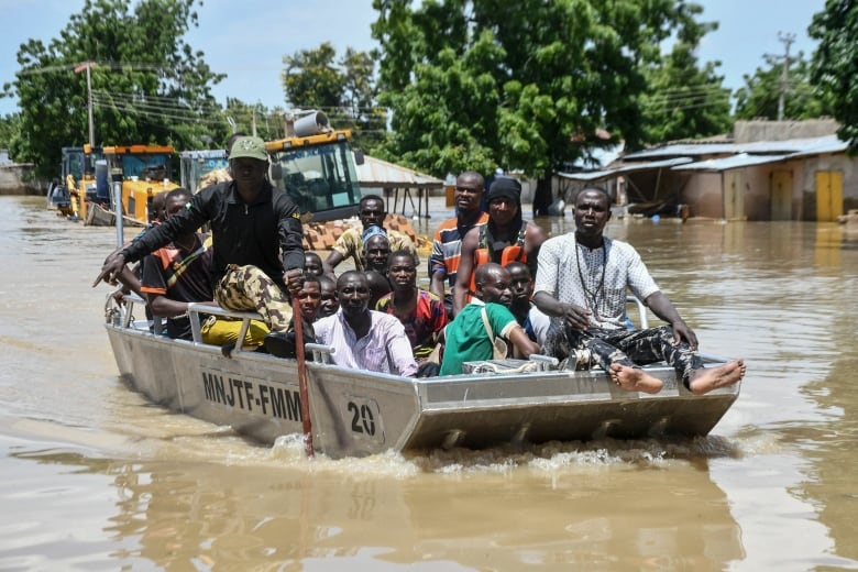 A dozen or so people are crammed aboard a small motor boat making its way through streets flooded with brown water.