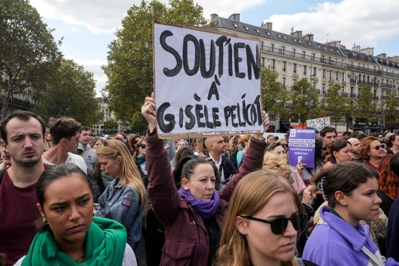 A group of people  stand in the street holding signs in french that say support for Gisele Pelicot