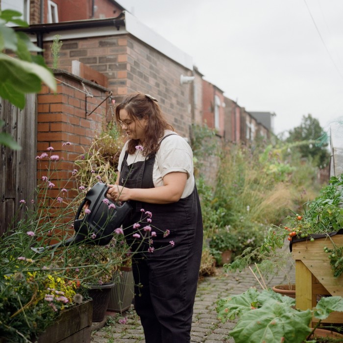 A woman watering a plant pot in an alleyway