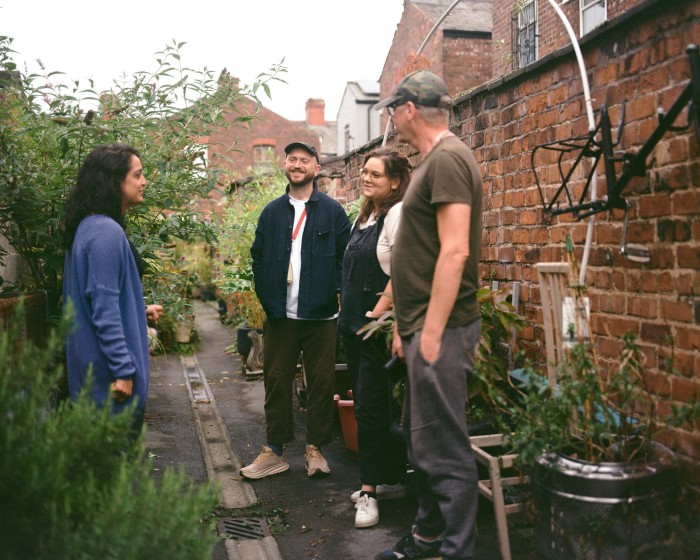 Two men and two women gather in an urban alleyway in Manchester, surrounded by plants and flowers