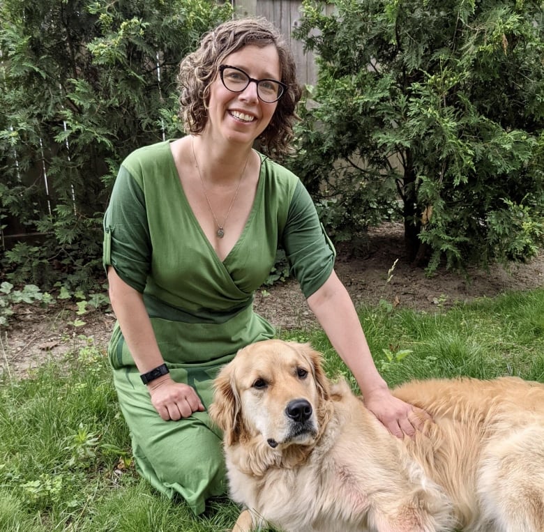 A woman wearing a green dress is sitting on green grass with a golden retriever dog. 