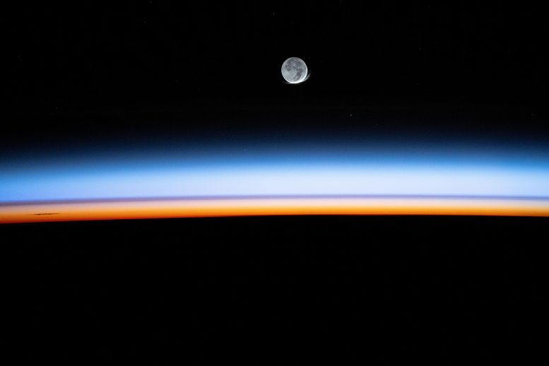 New Moon Begins Setting Behind Earth’s Colorful Atmosphere